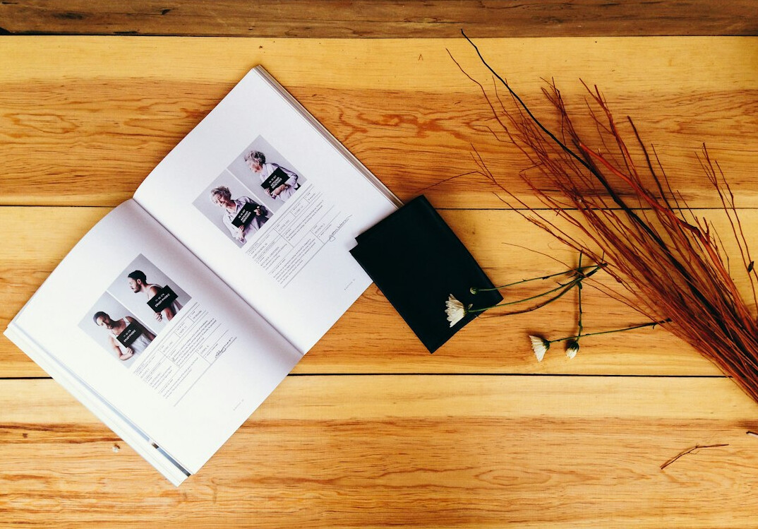 Overhead view of a wooden desk with a camera, notebook and printed photographs